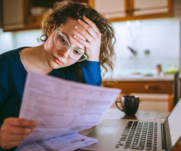 Young brunette curly female reading her bill papers, looking stressed